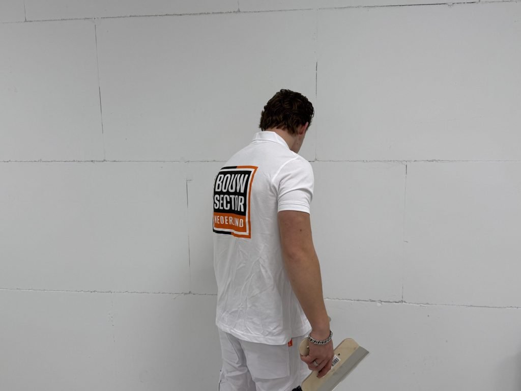 Stukadoor met plakspaan in de hand bekijkt een wand van lichte platen van dichtbij