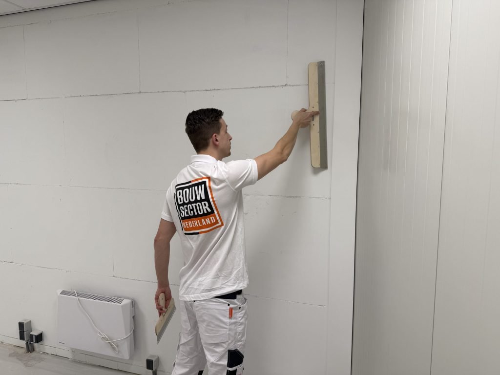 Stukadoor van Bouwsector Nederland strijkt met een lange spaan over een wand boven de kachel