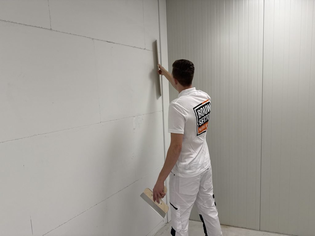 Stukadoor houdt de spaan verticaal tegen de naad van een wand van grote platen