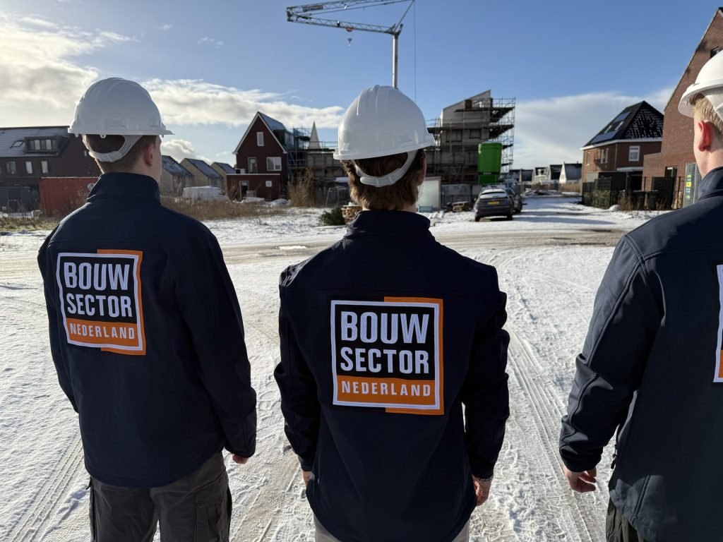 Drie vakmensen van Bouwsector Nederland met witte helm kijken naar de gevels van nieuwe woningen