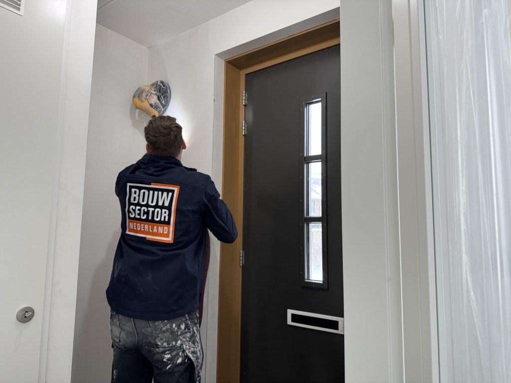 Vakman van Bouwsector Nederland schuurt met een langnekschuurmachine boven een voordeur