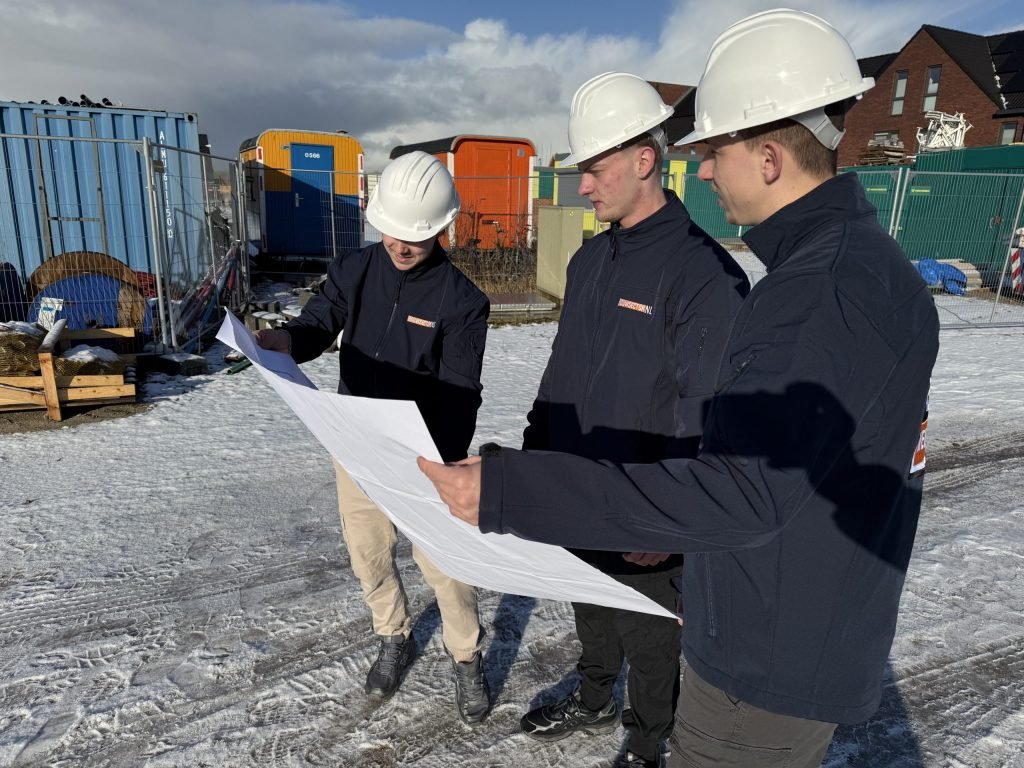 Drie vakmensen van Bouwsector Nederland met witte helm overleggen bij een uitgevouwen bouwtekening